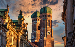Frauenkirche in München bei Sonnenuntergang mit dramatischem Himmel im Hintergrund.